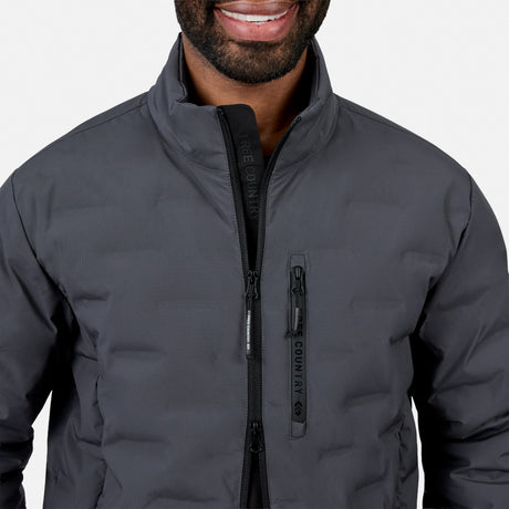 [Model is wearing size M.] A close-up of a man wearing a dark gray Country Life puffer jacket, showing the front zipper, stand-up collar, and a vertical zippered pocket on the chest.