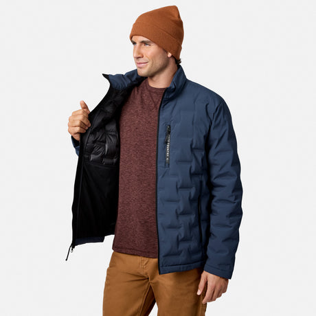 [Model is wearing size M.] A man wearing a navy blue insulated puffer jacket with a black interior lining, a rust-brown knit beanie, a maroon heathered sweater, and brown pants, standing against a light gray studio background.