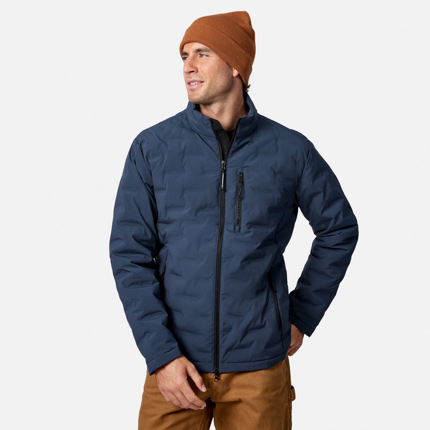 [Model is wearing size M.] A man wearing a navy blue puffer jacket, a rust-orange beanie, and brown pants, standing against a light gray studio background.