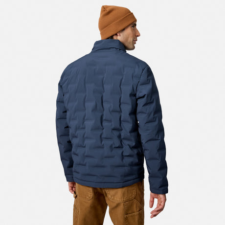 [Model is wearing size M.] A man wearing a navy blue quilted puffer jacket, a brown knit beanie, and brown pants, shown from the back against a light gray studio background.