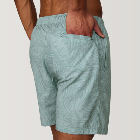 A person seen from the back with one hand in a pocket, wearing Clearance Men's Palm Heaven Swim Short in light green recycled polyester with a subtle leaf pattern.