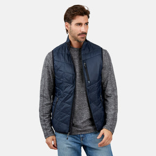 [Justin is 6’1” wearing a size Medium.] Man wearing the Free Country Men's FreeCycle® Stimson Puffer Vest in navy, featuring quilted design, REPREVE® poly fill, and a vertical zip, layered over a grey long-sleeve shirt with light jeans.