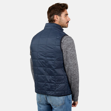 [Justin is 6’1” wearing a size Medium.] Man wearing the Free Country Men's FreeCycle® Stimson Puffer Vest in navy, featuring quilted design, REPREVE® poly fill, and a vertical zip, layered over a grey long-sleeve shirt with light jeans.