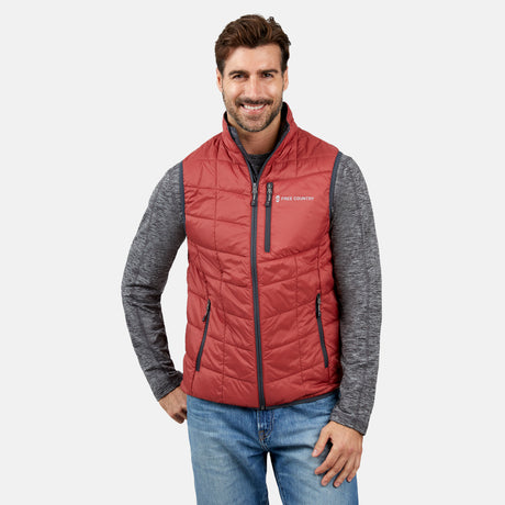[Justin is 6'1" wearing a size Medium.] Man wearing the Free Country Men's FreeCycle® Stimson Puffer Vest in red, featuring quilted design, REPREVE® poly fill, and a vertical zip, layered over a grey long-sleeve shirt with light jeans.