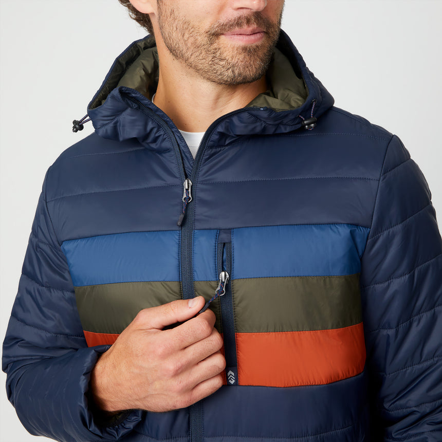 [Matt is 6'2" wearing size M.] Men’s Free Country zip-front puffer jacket in navy with multicolored horizontal chest stripes—featuring full-length zipper closure, insulated design, and classic hood-free silhouette. Paired with a white shirt and blue jeans for a vibrant, cold-weather look with retro-inspired flair.
