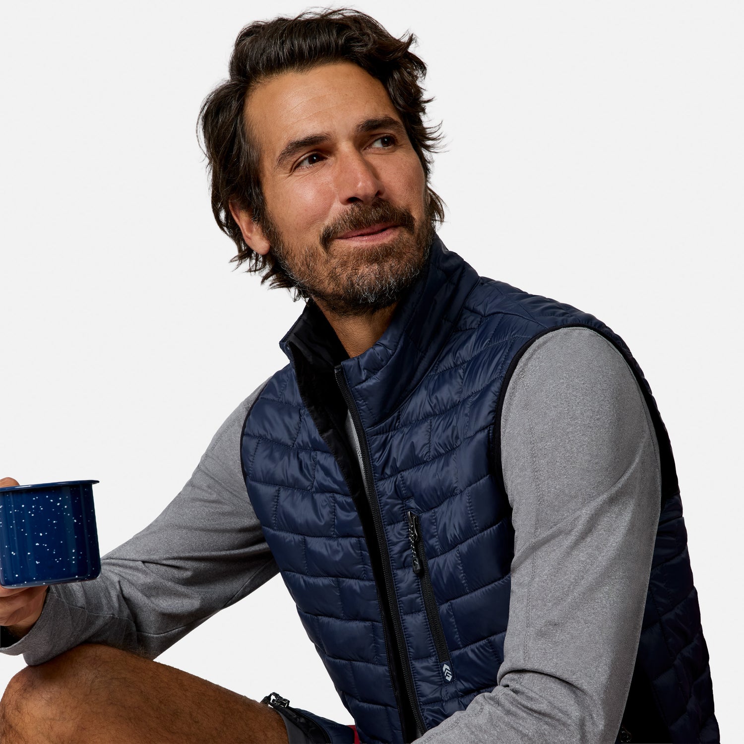 [Model is wearing size M.] A man wearing a navy blue quilted puffer vest over a gray long-sleeve shirt, holding a blue enamel mug against a plain white background.