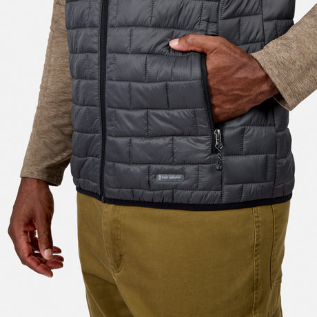[Model is wearing size M.] Close-up of a person wearing a dark gray quilted puffer vest over a beige long-sleeve shirt and olive pants, with one hand in the vest's pocket. A small Patagonia logo patch is visible near the lower front.