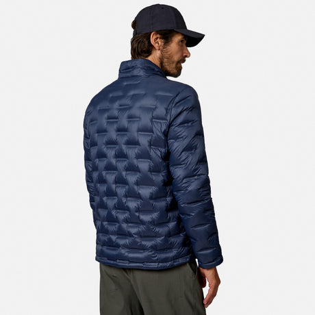 [Model is wearing size M.] A man wearing a navy blue quilted puffer jacket, a dark navy baseball cap, and olive green pants, shown from a rear three-quarter view against a light gray studio background.