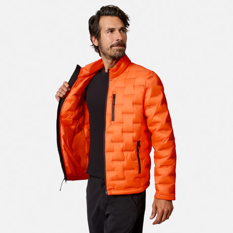 [Model is wearing size M.] A man wearing a bright orange quilted puffer jacket over a black shirt, shown from the waist up against a light gray studio background. He is holding the jacket open with one hand.