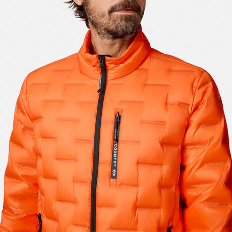 [Model is wearing size M.] A close-up of a man wearing a bright orange quilted puffer jacket with a black front zipper and a vertical zippered pocket featuring a black brand tab that reads Free Country.
