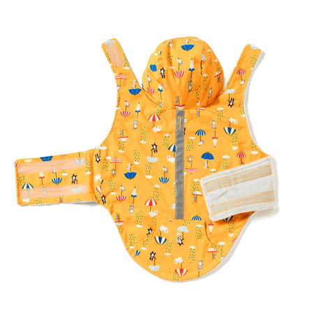 The Free Country Dog Raincoat is bright yellow with a beach umbrella and chair pattern, adjustable Velcro straps, and a reflective strip down the center, shown laid flat on a white background.