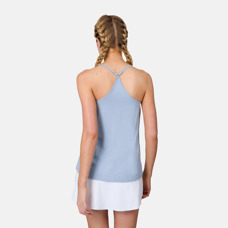 A woman with blonde braided hair stands with her back to the camera, wearing a Free Country Women's Microtech® Chill B Cool V-Neck Cami Top with Built-In Bra in light blue and a white skirt, set against a plain white background.