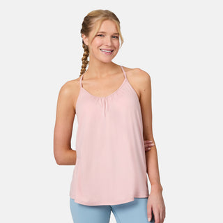 A smiling woman with braided hair wears the Free Country Women's Microtech® Chill B Cool V-Neck Cami Top with Built-In Bra in light pink and light blue pants, standing against a plain white background.