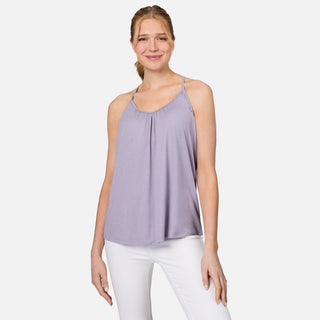 A woman with light brown hair in a ponytail is smiling and wearing the Free Country Women's Microtech® Chill B Cool V-Neck Cami Top with Built-In Bra in light purple and white pants, standing against a plain white background.