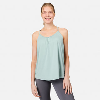 A woman wearing a Free Country Women's Microtech® Chill B Cool V-Neck Cami Top with Built-In Bra in light green and gray leggings stands smiling against a plain white background.