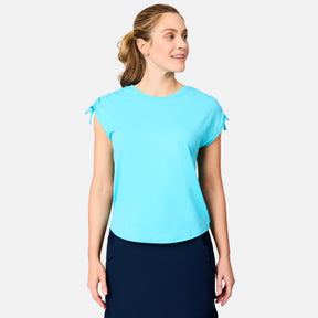 A woman with light brown hair in a ponytail smiles while wearing a light blue Free Country Women's Microtech® Chill Dolman Sleeve Top and a navy skirt, facing slightly to the side against a plain background.