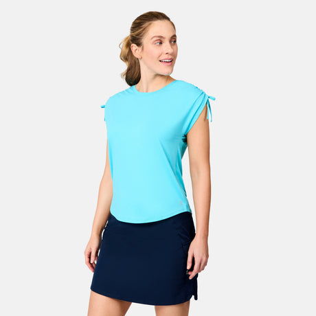 A woman stands against a plain background in a light blue Free Country Women's Microtech® Chill Dolman Sleeve Top and a navy skirt, smiling as she enjoys the UPF 50+ protection her outfit provides.
