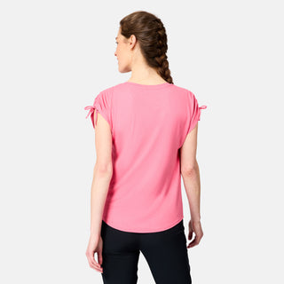 A woman with braided hair faces away from the camera, wearing a pink Free Country Women's Microtech® Chill Dolman Sleeve Top and black pants against a plain light background.