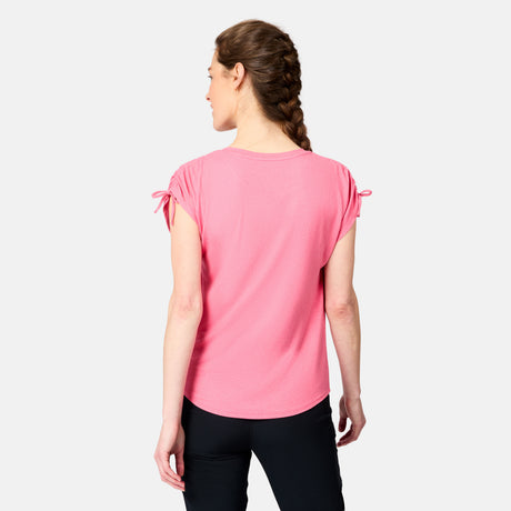 A woman with braided hair faces away from the camera, wearing a pink Free Country Women's Microtech® Chill Dolman Sleeve Top and black pants against a plain light background.