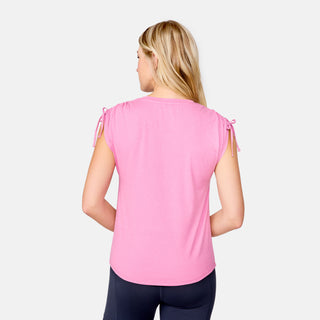 A woman with long blonde hair is shown from the back, wearing a pink Free Country Women's Microtech® Chill Dolman Sleeve Top with tied shoulders and black leggings, standing against a plain light background.