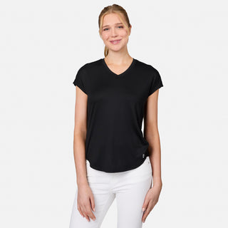 A smiling blonde woman in a ponytail wears the Free Country Women's Microtech® Chill B Cool Tee, a black short-sleeve V-neck moisture-wicking shirt, with white pants, standing against a plain white background.