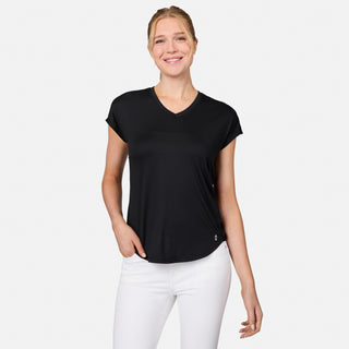 A woman smiles against a white background, wearing the Free Country Women's Microtech® Chill B Cool Tee in black with white pants, her hand in her pocket.