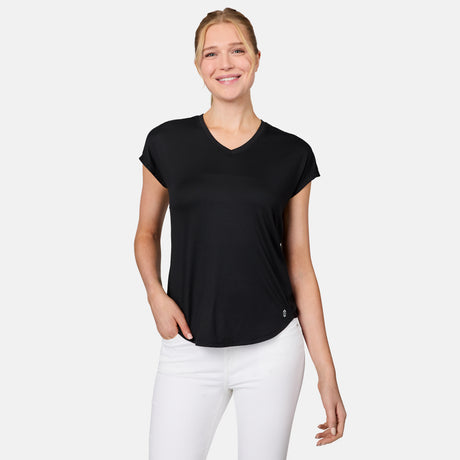 A woman smiles against a white background, wearing the Free Country Women's Microtech® Chill B Cool Tee in black with white pants, her hand in her pocket.