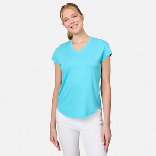 A smiling woman with blonde hair in a loose ponytail wears the Free Country Women's Microtech® Chill B Cool Tee in turquoise and white pants, standing against a plain white background.
