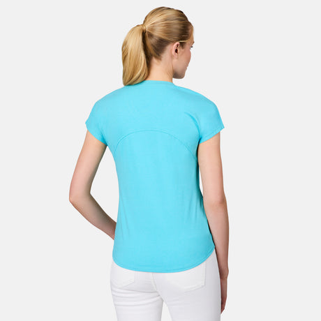 A woman with blonde hair in a ponytail stands with her back to the camera, wearing the Free Country Women's Microtech® Chill B Cool Tee in light blue and white pants, set against a plain white background.