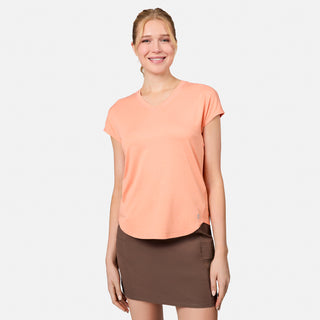 A smiling woman stands against a plain background, wearing the Free Country Women's Microtech® Chill B Cool Tee in peach and a brown skirt.