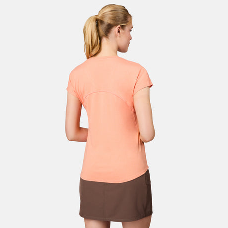 A woman with blonde hair in a ponytail faces away, wearing the Free Country Women's Microtech® Chill B Cool Tee in peach and a brown skirt, set against a plain light gray background.