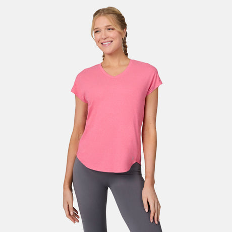 A smiling woman with blonde braided hair wears the Free Country Women's Microtech® Chill B Cool Tee in pink and gray leggings, standing against a plain white background.