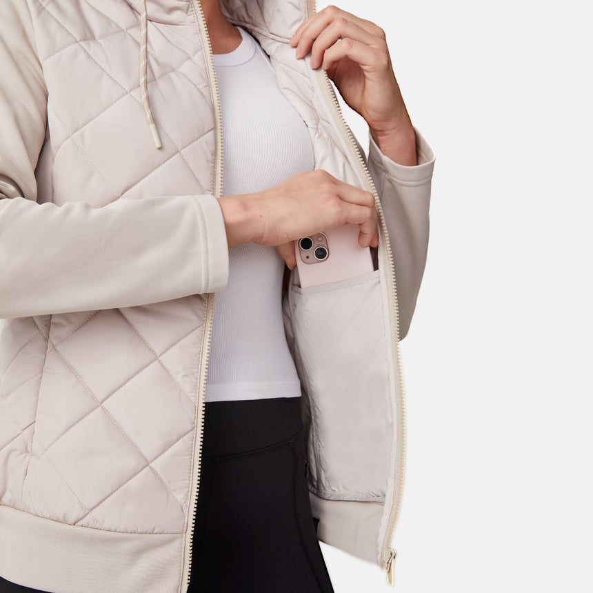 [Emily is 5'9" wearing size S.] Women’s light-colored quilted jacket with diamond-pattern stitching, zip-front closure, hood, and zippered pockets—layered over a white long-sleeve shirt and styled with black pants for a casual, cool-weather look.
