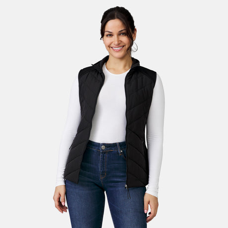 [Model is wearing a size Small.]  Woman wearing the Free Country Women's Quilted Hybrid Vest in black, featuring a unique quilted design with stretch knit panels and REPREVE® synthetic fill.