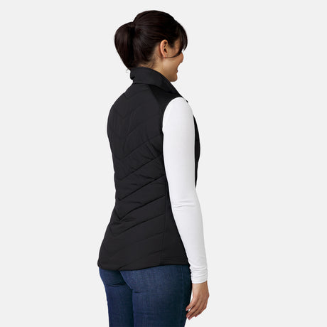[Model is wearing a size Small.] Woman wearing the Free Country Women's Quilted Hybrid Vest in black, featuring a unique quilted design with stretch knit panels and REPREVE® synthetic fill.