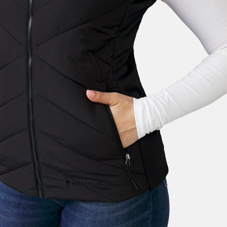 [Model is wearing a size Small.] Woman wearing the Free Country Women's Quilted Hybrid Vest in black, featuring a unique quilted design with stretch knit panels and REPREVE® synthetic fill.