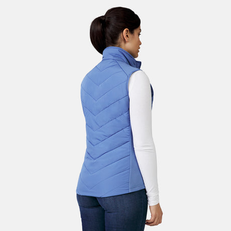[Model is wearing a size Small.]  Woman wearing Free Country Women's Quilted Hybrid Vest in blue  with a full front zipper opening, patterned quilting, lower pocketse, and water resistant and wind resistant stretch performance fabric. light grey background. Perfect women’s jacket for winter weather.