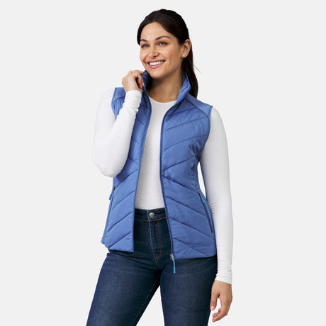 [Model is wearing a size Small.]  Woman wearing Free Country Women's Quilted Hybrid Vest in blue  with a full front zipper opening, patterned quilting, lower pocketse, and water resistant and wind resistant stretch performance fabric. light grey background. Perfect women’s jacket for winter weather.