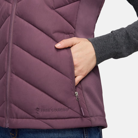 Close-up of a person wearing a plum-colored Free Country Women’s Quilted Hybrid Vest featuring a zippered pocket and a logo near the hem.