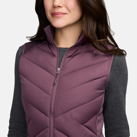 A person wearing a purple Free Country Women’s Quilted Hybrid vest over a dark gray long-sleeved shirt.