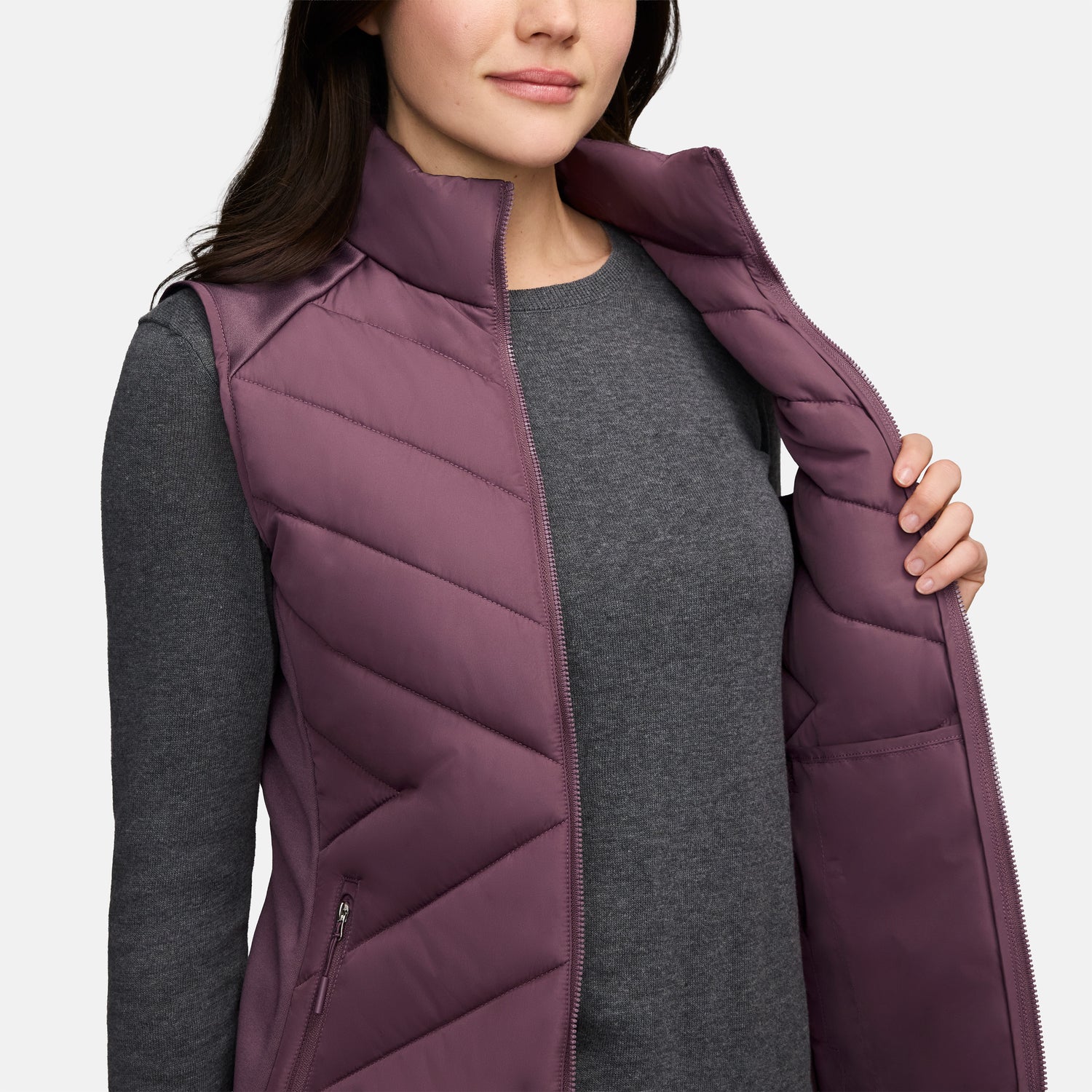 A person wears a plum-colored Women’s Quilted Hybrid Vest with REPREVE synthetic fill over a gray long-sleeved shirt, holding the zipper open with one hand.