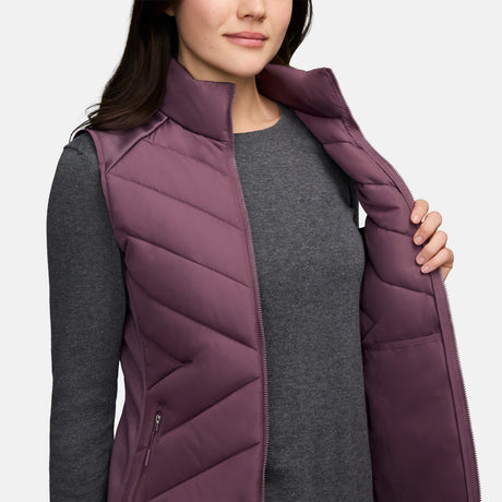 A person wears a plum-colored Women’s Quilted Hybrid Vest with REPREVE synthetic fill over a gray long-sleeved shirt, holding the zipper open with one hand.