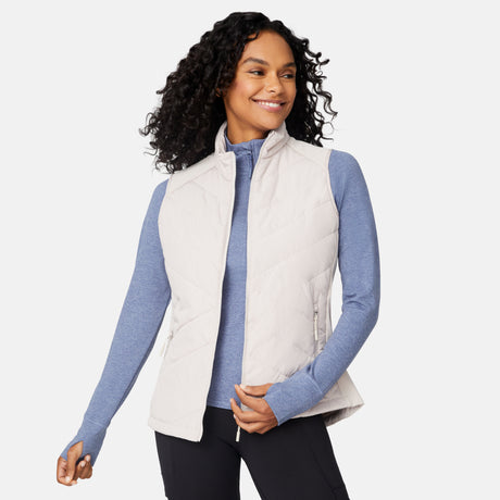 [Angelique is 5'10" wearing size S.] Woman wearing a beige puffer vest over a blue long-sleeve shirt on a white background