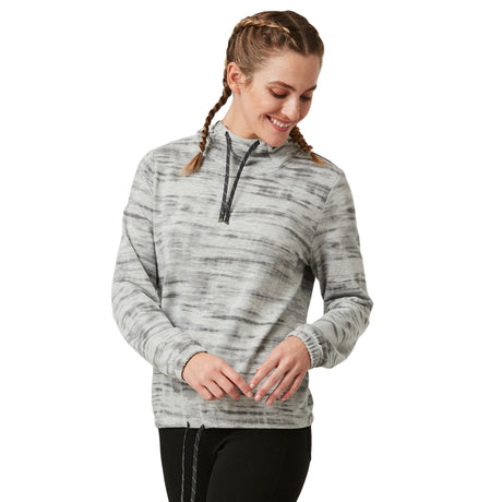 A woman with braided hair smiles while looking down, wearing the Clearance Women's Luxe Easy Fit Pullover in light gray with subtle stripes and black pants. The long-sleeve, quarter-zip top adds comfort and style against a plain white background.