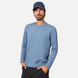 [Model is wearing size M.] A man wearing a heathered blue long-sleeve crewneck shirt, a navy blue baseball cap, and dark pants, standing against a light gray studio background.