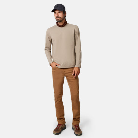 [Model is wearing size M.] A man modeling a light beige long-sleeve turtleneck sweater, paired with brown pants, brown hiking boots, and a dark navy baseball cap, against a light gray studio background.
