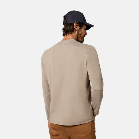 [Model is wearing size M.] A man wearing a light beige long-sleeve crewneck shirt, brown pants, and a navy blue baseball cap, shown from the back against a plain light gray background.