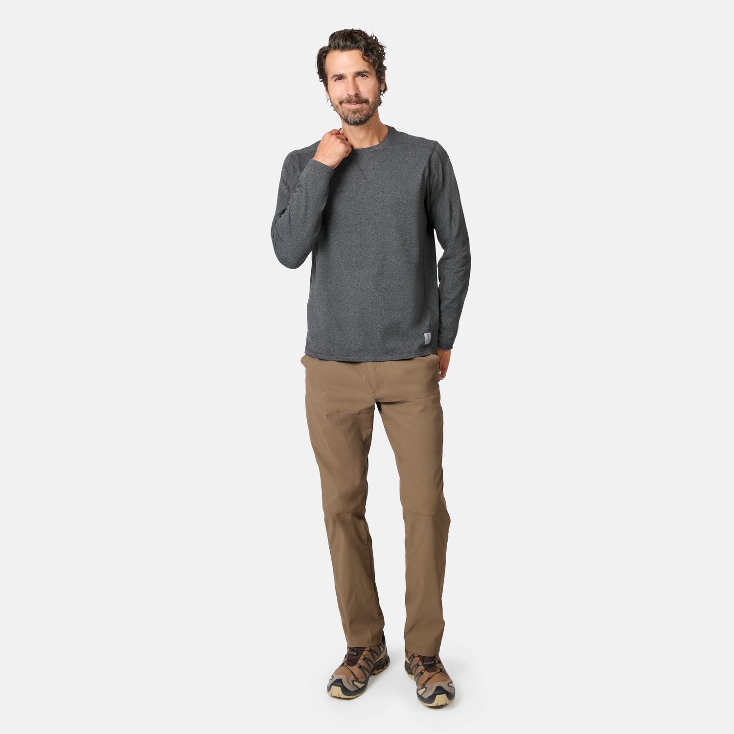 [Model is wearing size M.] A man modeling a dark gray long-sleeve crewneck shirt and brown pants against a light gray studio background.