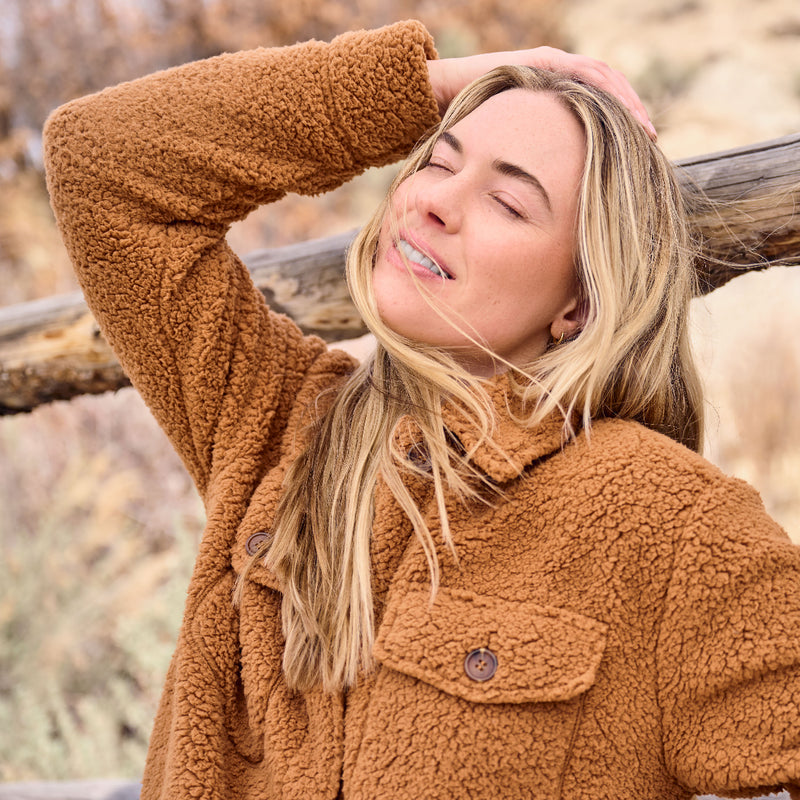 Woman wearing a brown fleece jacket outdoors with a blurred natural background