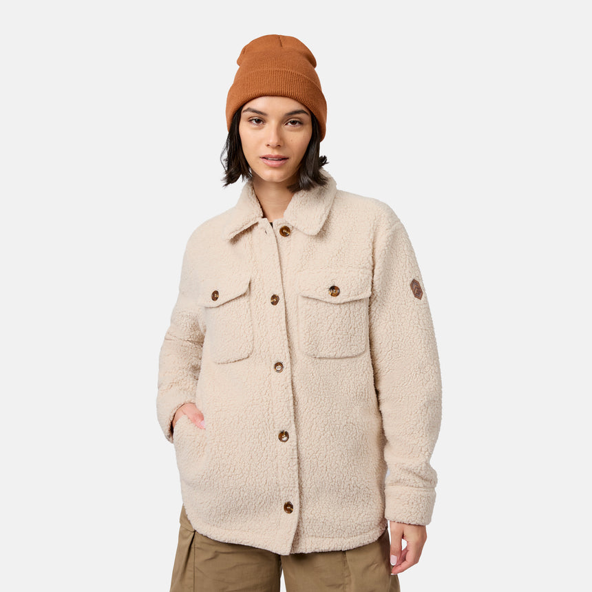 [Model is wearing size S.] A woman wearing a beige sherpa fleece button-up jacket with brown buttons, paired with brown pants and an orange-brown beanie, photographed against a light gray studio background.